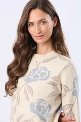 Buzo tejido en jacquard con estampado floral en tonos azul y marrón sobre base color crema. Presenta cuello redondo y puños acanalados.