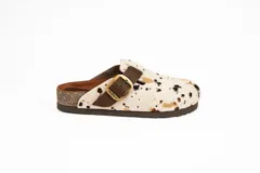 Zueco con capellada de pelo de vaca con manchas marrones y negras sobre base blanca, plantilla anatómica de cuero y hebilla lateral ajustable.