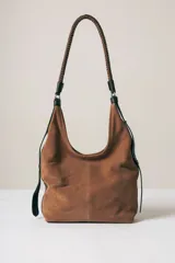 Cartera tipo hobo de gamuza color marrón, con correa trenzada de cuero negro y detalles laterales en cuero negro.