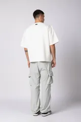 Remera de corte oversize color beige, con cuello redondo y etiqueta decorativa pequeña en el ruedo inferior.