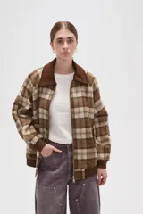 Campera de estilo bomber con cierre frontal, confeccionada en tejido a cuadros en tonos marrones y beige. Presenta cuello camisero en pana marrón, puños y ruedo elásticos acanalados, y bolsillos laterales.