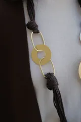Collar largo de diseño artesanal compuesto por múltiples hilos de cordón color chocolate, con nudos decorativos y eslabones metálicos circulares y ovalados en tonos dorado y plateado.