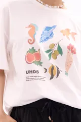 Remera blanca de manga corta, corte oversize, con estampa colorida de motivos marinos y botánicos en el frente.