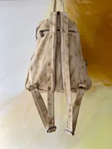 Mochila de cuero de Carolina De Cunto, modelo Lucy Natu Gold Arte. Presenta combinación de tonos naturales y dorados con textura efecto cocodrilo, diseño frontal intervenido con arte pintado a mano y bolsillo vertical con cierre.