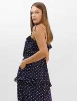Vestido largo azul marino con estampado de lunares blancos, confeccionado en gasa fluida. Cuenta con tirantes finos ajustables con lazos en los hombros, escote con volados, corte en la cintura con lazo ajustable, y falda larga con múltiples capas y volados horizontales.