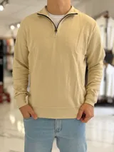 Buzo de punto color beige con cuello alto y medio cierre frontal, mangas largas y puños y cintura elásticos acanalados.