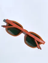 Lentes de sol con armazón de marco completo en color gris mate, con detalles decorativos en color rojo en las esquinas y patillas. Cuentan con cristales oscuros polarizados con protección UV 400.