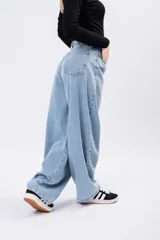 Jean de tiro alto con corte barrel leg, estilo globo, confeccionado en denim de tono azul claro. Presenta costuras reforzadas en la zona de las rodillas y un diseño de pierna ancha que se estrecha sutilmente hacia el tobillo.
