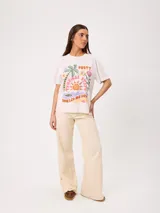 Remera de algodón marca Rusty, color blanco, de corte holgado, con cuello redondo, mangas cortas y estampado frontal colorido de temática tropical.