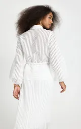 Camisa de rayas verticales blanca de Le Lis Blanc, modelo Regina, confeccionada en tejido fluido con ligera transparencia. Presenta corte recto, cuello clásico, mangas largas con volumen y puños ajustados, cierre frontal de botones y detalle fruncido con cordón en la cintura.