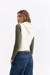 Chaleco de punto color beige, de corte corto y holgado. Presenta capucha, cierre frontal completo y terminaciones acanaladas en la cintura.