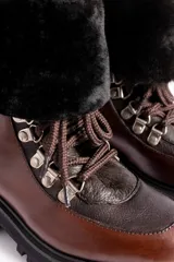 Borcegos de cuero vacuno en tonos marrón, con diseño de caña media y cuello con forro de piel sintética negra. Presentan cordones marrones, ganchos metálicos para ajuste y suela de goma tipo track con plataforma.