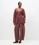 Cardigan de tricot en color borravino, con textura acanalada, escote en V profundo y cierre frontal con un único botón metalizado. Presenta mangas largas y un diseño alargado con amarre ajustable en la espalda.