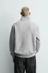 Sudadera de corte regular con cuello subido y cierre frontal de cremallera. Presenta mangas largas, puños y ruedo en rib, y bordados decorativos a contraste en el frente.