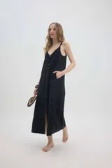 Vestido largo negro de lino, con silueta tipo lencera, escote en V con detalle de encaje, tirantes regulables y una hilera de botones frontales decorativos. Cuenta con bolsillos laterales.