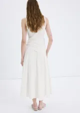 Vestido midi color blanco con diseño evasé, cuello redondo y sin mangas de tirante ancho. Cuenta con un detalle de pañuelo bordado en la cintura con cierre de cremallera lateral.