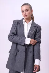 Blazer de corte sastrero en color gris con textura jaspeada. Presenta un diseño de doble botonadura, solapas clásicas y detalle de strass aplicado en una de las solapas. Cuenta con bolsillos laterales con solapa y mangas largas.