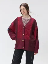Cardigan de punto grueso con diseño de bloques de color en tonos bordó y rojo. Presenta cuello en V, cierre frontal con botones, mangas largas abullonadas y parches decorativos en el pecho y hombro. Posee un calce oversize.