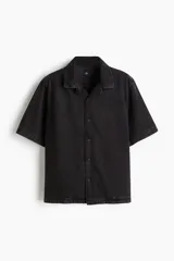 Camisa de denim negro, corte regular fit, con cuello resort, manga corta, tapeta lisa y bajo recto.
