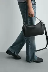 Bandolera negra de acabado liso, con compartimento principal con cierre de cremallera, bolsillos laterales planos y un bolsillo interior con cremallera. Incluye asa de mano extraíble y asa de hombro ajustable y extraíble.