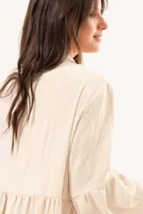 Vestido largo beige de silueta oversize, confeccionado en tela ligera con textura y motivos bordados tono sobre tono. Presenta escote en V, mangas amplias con volados y un gran volado en el ruedo.