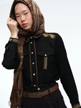 Camisa de color crudo con detalles de bordados en tonos mostaza y marrón en el cuello, hombros, bolsillos frontales y puños. Presenta cierre frontal con botones y dos bolsillos tipo cargo en el pecho.