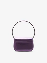 Bolso compacto tipo bandolera para mujer, con asa corta para llevar al hombro y correa desmontable opcional para usar cruzado. Confeccionado en cuero con acabado espejado brillante color morado. Presenta placa oval D galvanizada en la solapa.