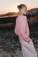 Sweater de punto color rosado con cuello redondo y manga larga, de bajo asimétrico con acabados en rib.