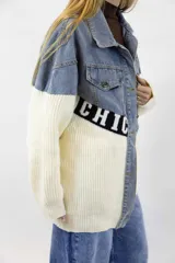 Campera oversize combinada de denim azul en la parte superior y tejido de punto blanco en la parte inferior, con una franja negra con letras blancas en el centro. Cuenta con cierre frontal de botones metálicos y bolsillos en el pecho.