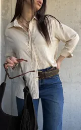 Camisa beige de manga larga con detalles bordados en la botonera y el cuello, cierre frontal con botones y diseño fluido.