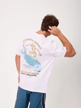 Remera Rusty de corte holgado, color amarillo, con estampa en la espalda de un personaje surfeando sobre un pez y textos descriptivos.