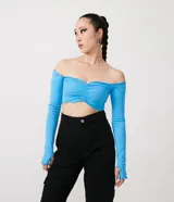 Blusa cropped de media malla color celeste, con escote hombro a hombro, mangas largas con abertura para los dedos y volantes en el escote, puños y bajo.