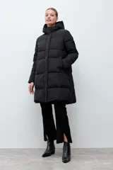 Campera puffer larga de color negro, con diseño capitoneado, capucha integrada y cierre frontal oculto. Presenta cierres laterales en el ruedo para mayor comodidad.