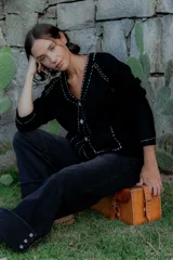 Saco tipo cárdigan negro de punto, con cuello en V y cierre frontal de botones. Presenta detalles de pespuntes decorativos en color blanco a lo largo del cuello, la botonera, los puños y los bolsillos frontales.