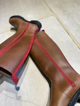 Bota de caña alta hasta la rodilla, confeccionada en cuero vacuno, con suela track de goma dentada y cierre lateral.