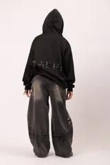 Pantalón de jean negro con proceso de lavado localizado, corte balloon fit de volumen curvo, detalles de bordados tipo costura expuesta y parches desflecados.