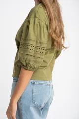 Remera de algodón color crudo con cuello redondo y mangas abullonadas de largo 3/4. Las mangas presentan detalles de encaje bordado y perforado con terminación elástica.
