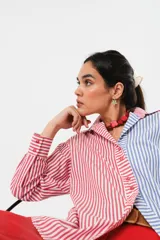 Camisa a rayas rojas y blancas en un lado y azules y blancas en el otro, con corte en A y abertura central con botonadura doble.