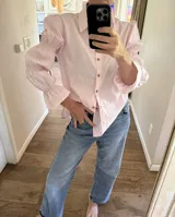 Camisa de algodón color rosado, de corte holgado, con cuello clásico, cierre frontal con botones y mangas largas abullonadas con detalles fruncidos.