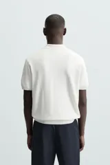 Jersey de punto color verde oliva, de calce relajado (relaxed fit), con cuello solapa y abertura frontal en forma de V. Es de manga corta y presenta acabados en rib en puños y ruedo.