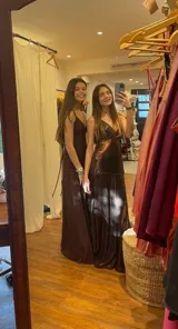 Vestido largo de satén color marrón con acabado metalizado, escote en V, tirantes finos cruzados en la espalda y diseño con corte bajo el busto y volados en la falda.