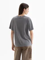 Remera gris con efecto lavado, de corte holgado y cuello redondo. Presenta una estampa frontal con motivos florales, un corazón central y la inscripción 'A love letter to winter flowers'. Cuenta con tajos laterales en el ruedo.