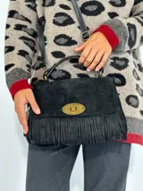 Cartera de mano negra de gamuza con flecos y cierre dorado.