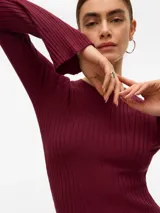 Vestido corto de tejido de punto acanalado en color bordó, con cuello redondo y mangas largas con terminación ligeramente acampanada. Presenta un diseño ajustado al cuerpo.