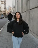 Canguro negro con capucha y cierre frontal, con texto bordado en el pecho y bolsillos laterales.