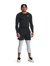 Calza deportiva de compresión tipo 3/4, color gris claro, con cintura elástica ancha negra con logo de la marca. Presenta paneles de malla para ventilación, bolsillo lateral y logo de Under Armour en la pierna.