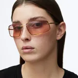 Lentes de sol rectangulares con montura de acero inoxidable color oro y lentes de nylon con degradado en tonos marrones. Presentan un diseño envolvente inspirado en los años 2000 con patillas de acetato.