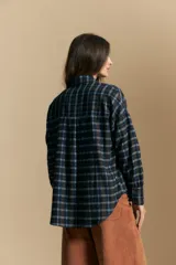 Camisa de estilo leñador con estampado de cuadros en tonos azul, negro y marrón. Presenta cuello clásico, cierre frontal con botones y mangas largas con puños abotonados.