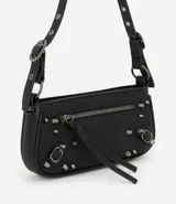 Cartera tipo baguette de PU color beige claro, con acabado liso y detalles de apliques metálicos tipo tachas y argollas en color gunmetal. Presenta un bolsillo frontal con cierre y un tirador de cuero sintético colgante. Incluye asa corta ajustable con hebilla.