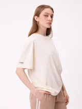 Remera de algodón con corte holgado, color crema, con estampado gráfico en la espalda que incluye un sol, montañas y mariposas con la frase Realities Rusty Collide.